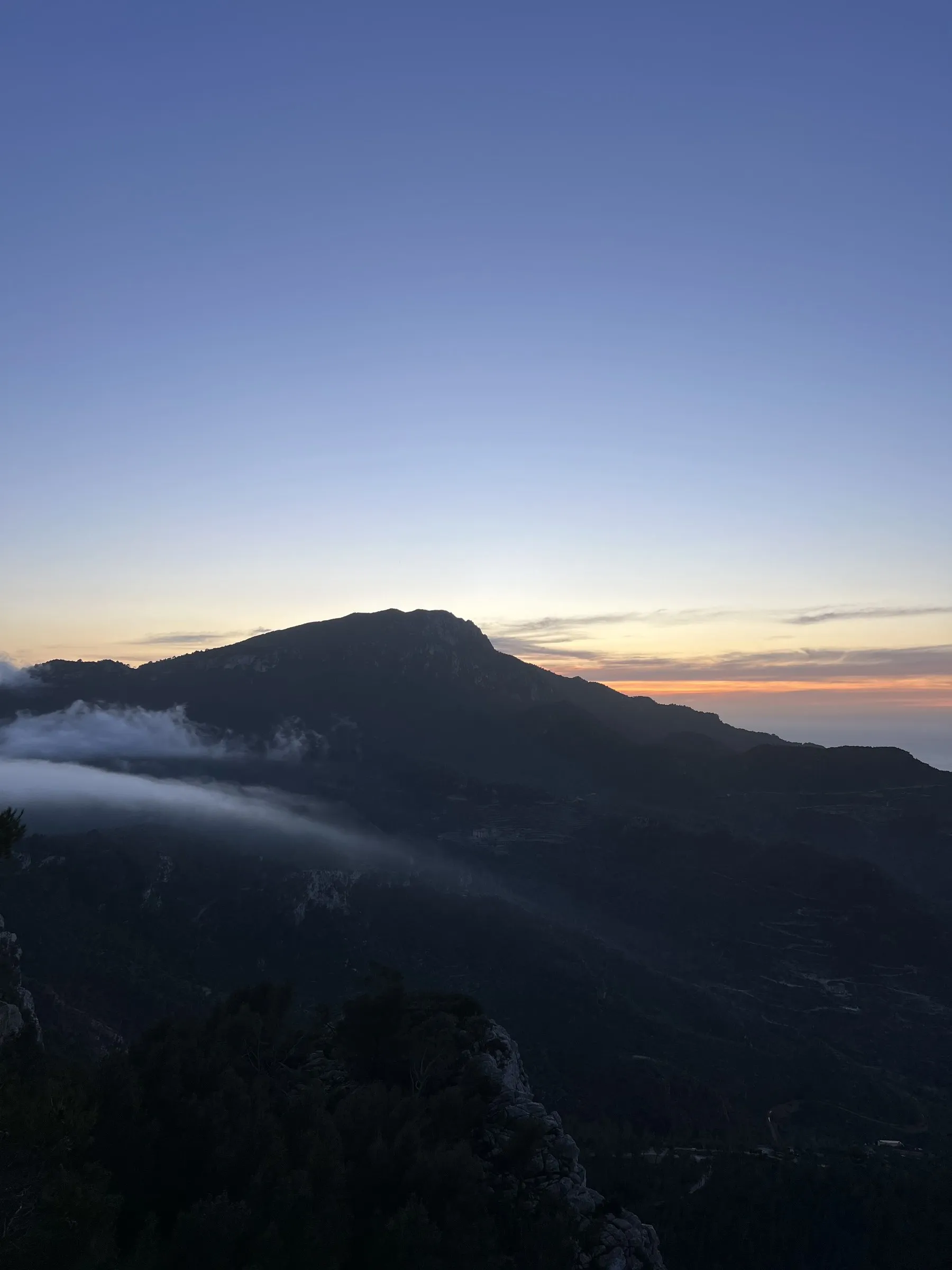 Ein Nebelband zieht bei Sonnenuntergang den Berghang über Banyalbufar hinunter.