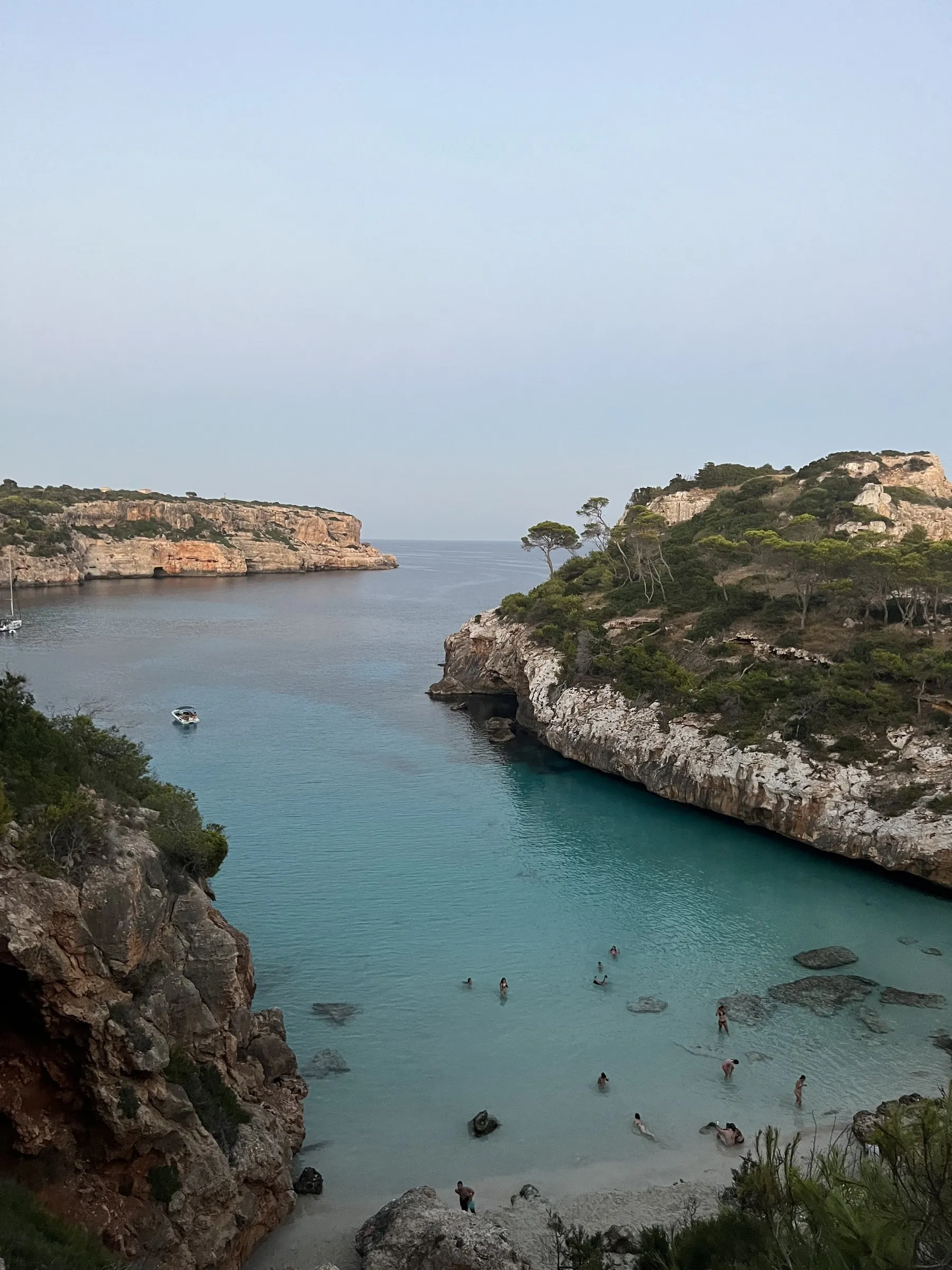 Der schmale Sandstreifen des Caló des Moro zwischen den Felswänden, mit Badenden im türkisfarbenen Wasser und einem ankernden Boot.