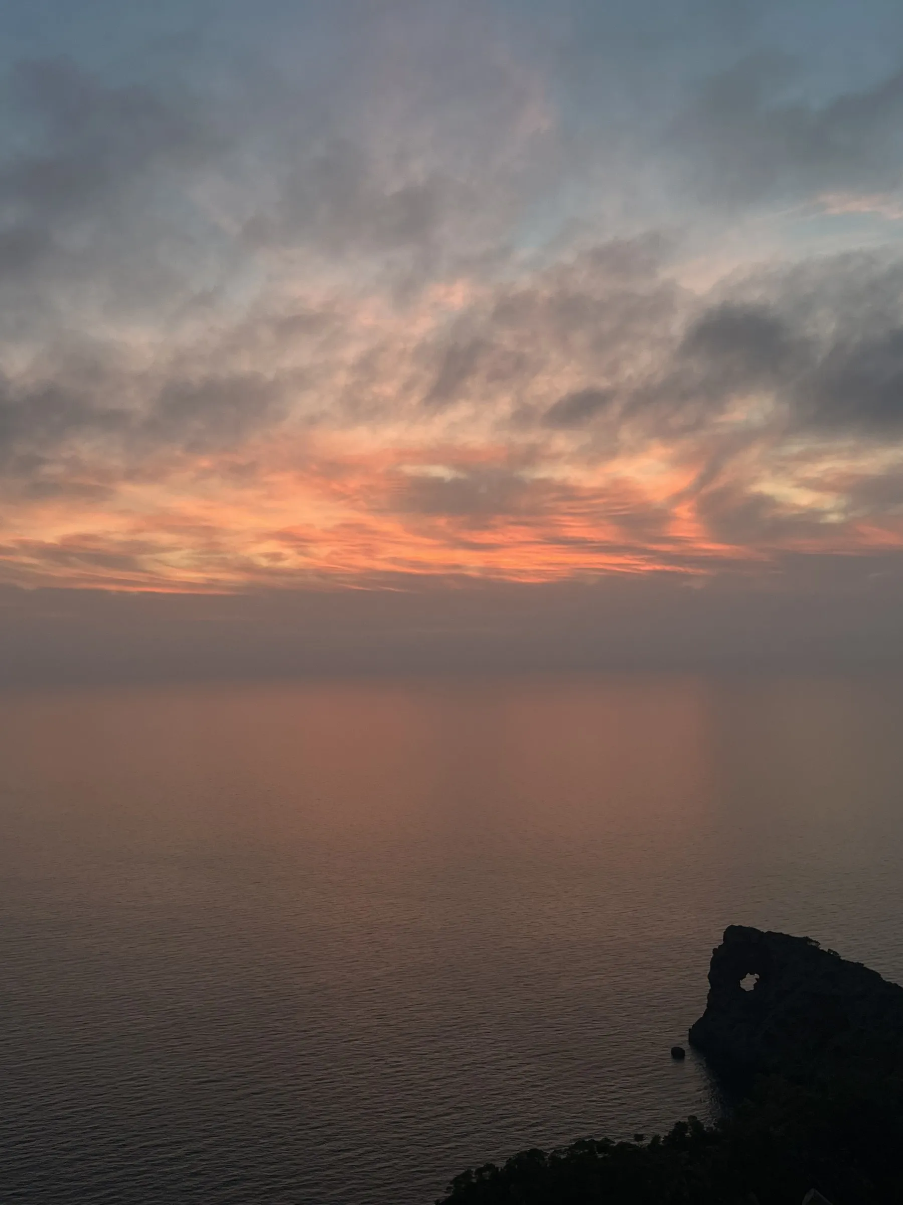 Oranje verlichte wolken boven een kalme zee bij zonsondergang op Cap de ses Salines.